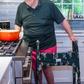 Man cooking in kitchen using a medical walker with a green and gray camouflage print walker cover on it. View highlights the tailored nature of the cover and the Jover logo on the front.