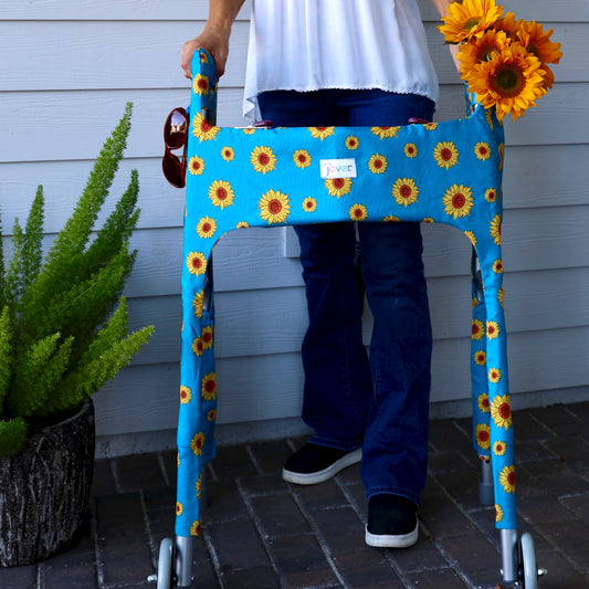 Person using a Sunflower Walker Cover on a standard folding walker with fresh sunflowers and sunglasses in the outside pockets.