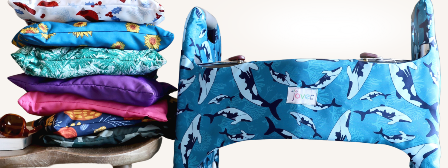 Stack of colorful Jover Walker Cover storage bags sitting on a stool with a whale-patterned walker cover on a walker standing beside it.