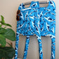 Blue whale patterned Jover walker cover with sunglasses and book in the cover pocket on a folded standard walker leaning against a wall next to a plant